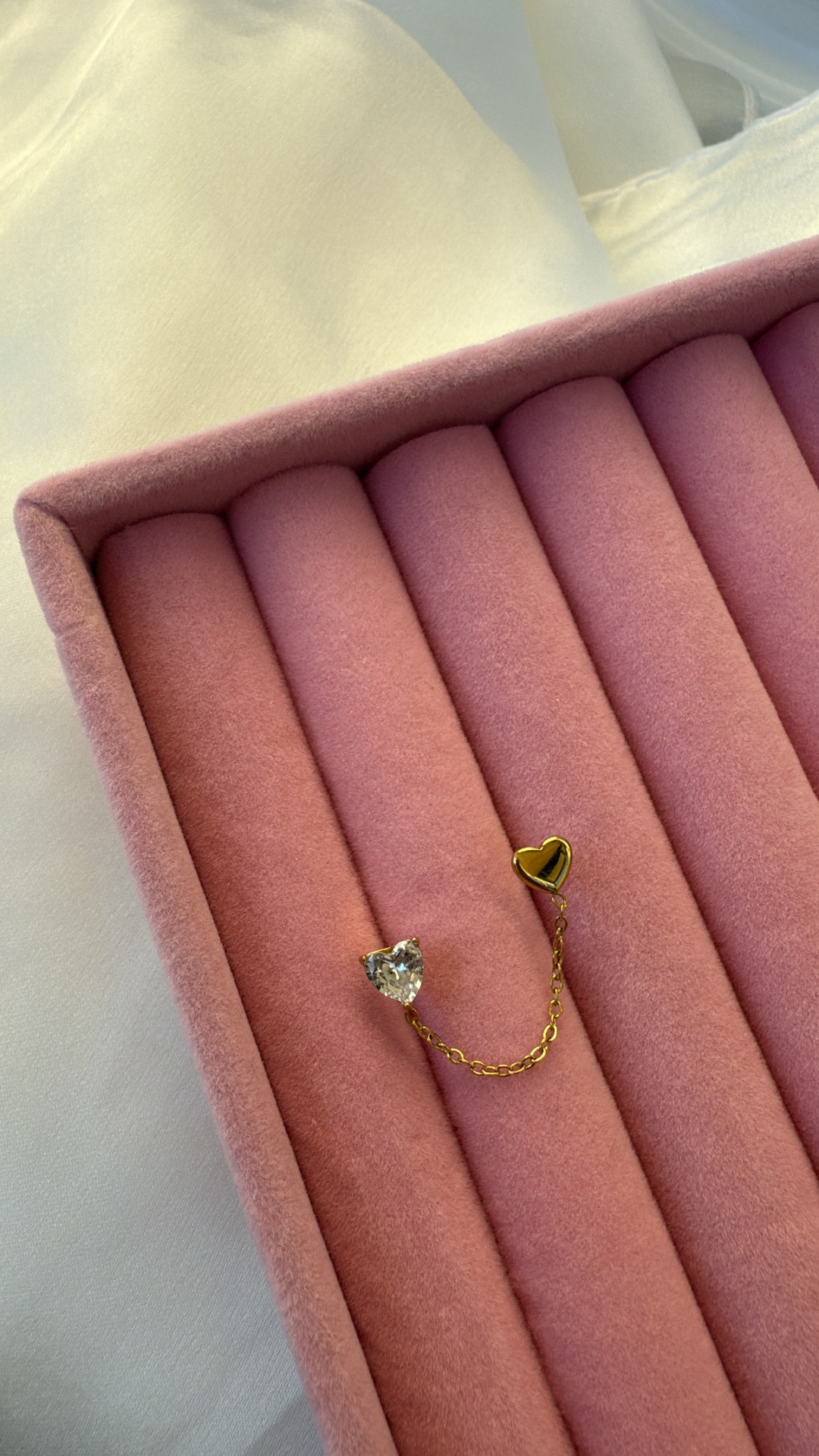 Brincos em forma de coração com corrente dourada numa caixa cor-de-rosa.