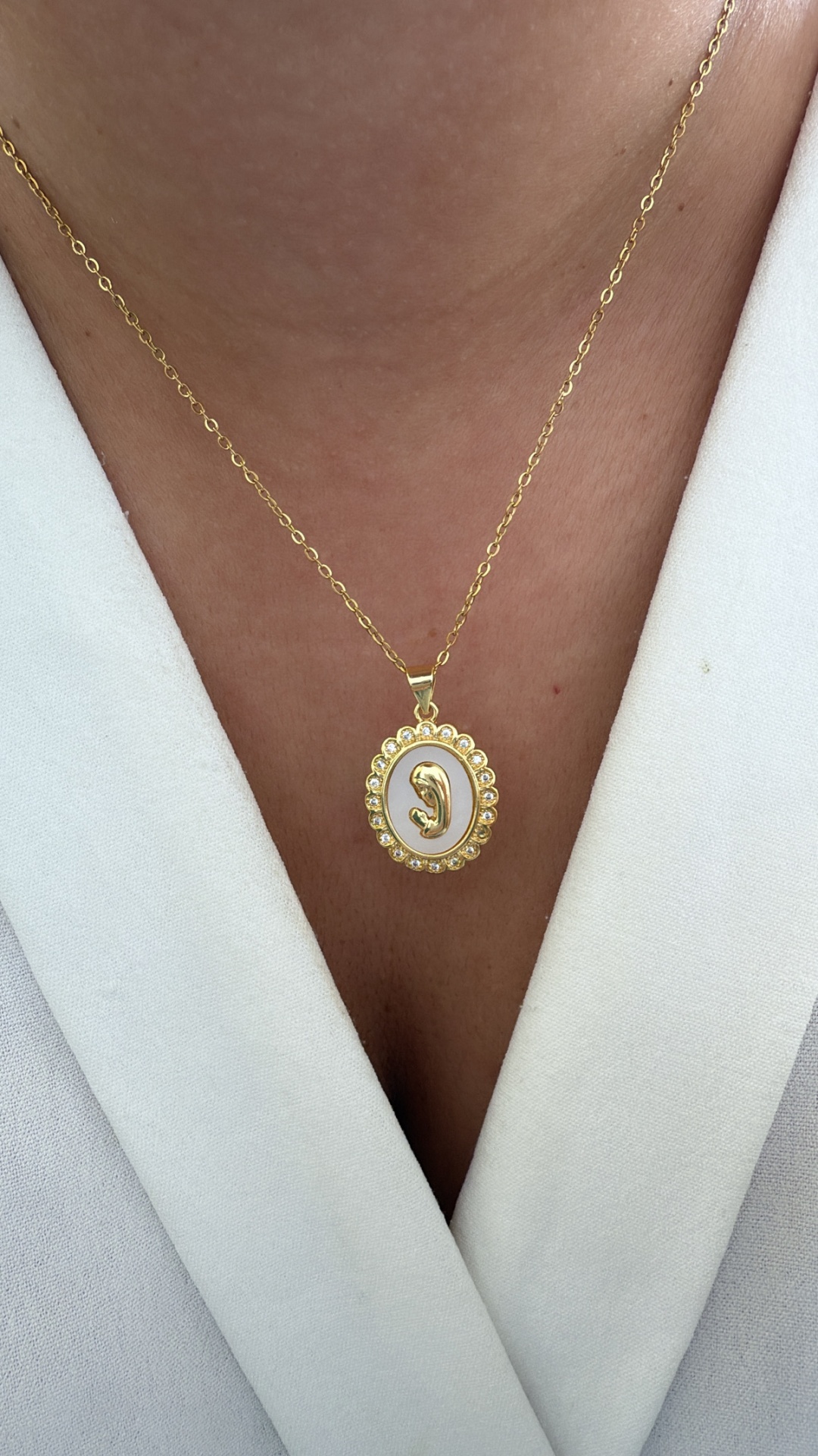 Colar dourado com pendente oval branco e letra G em cristais