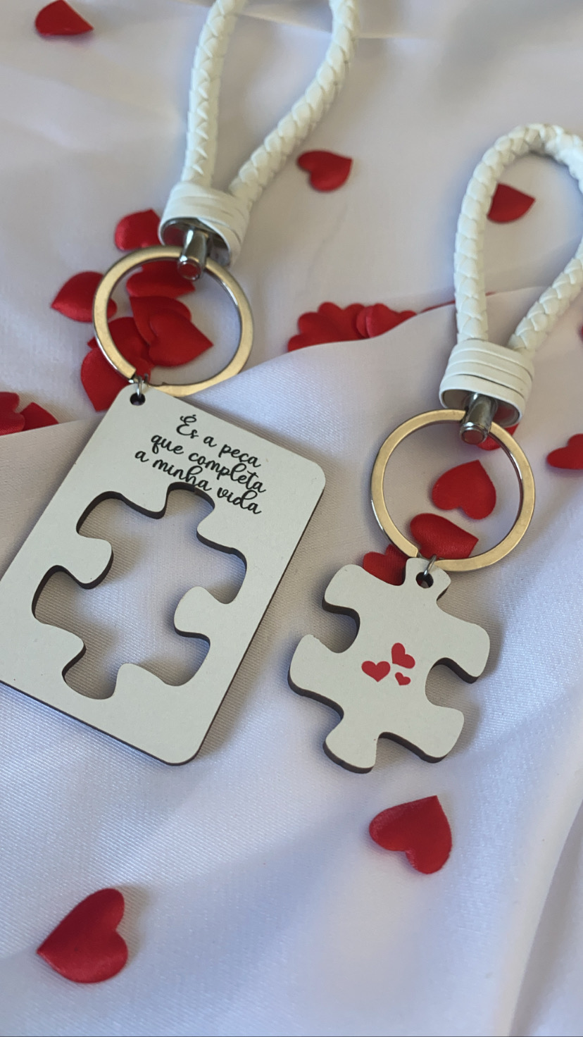 Conjunto de dois porta-chaves com peça de puzzle e cordão branco sobre tecido branco e corações vermelhos