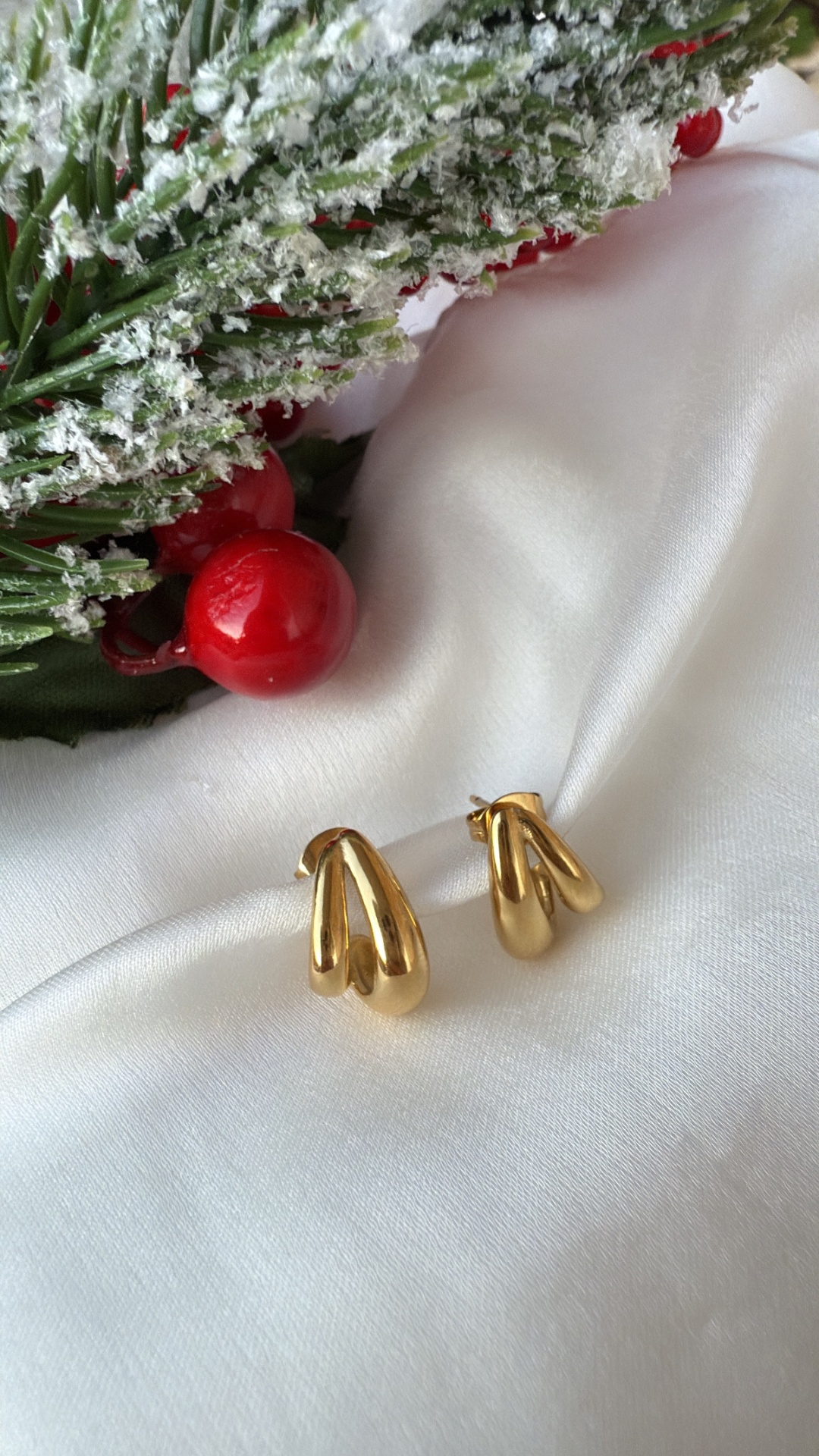 Brincos dourados sobre tecido branco com decoração natalícia