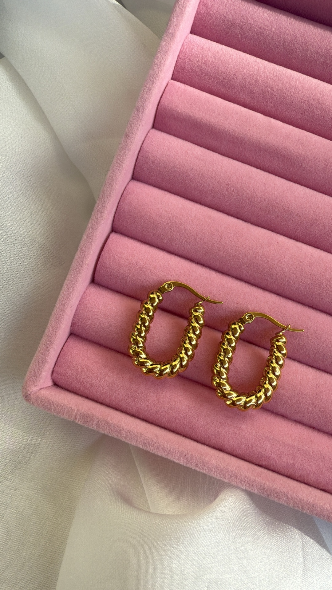 Brincos de argola dourados em caixa rosa de veludo com fundo branco