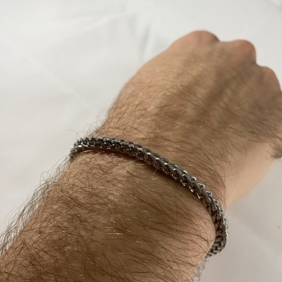 Pulseira de malha prateada no pulso de uma pessoa sobre fundo branco