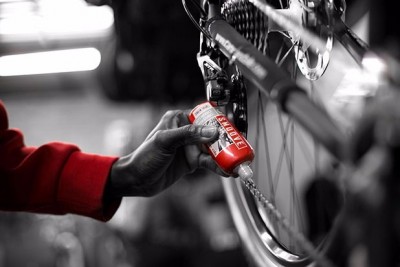 Pessoa a aplicar óleo lubrificante vermelho numa corrente de bicicleta