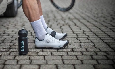 Sapatos de ciclismo brancos com fechos e garrafa preta 'fizik' ao lado