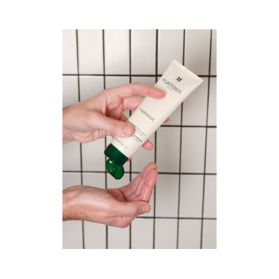 Tubo de creme RENE FURTERER TRIPHASIC com tampa verde aberto e mãos segurando.