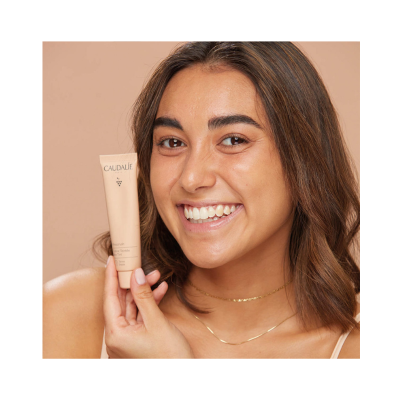 Mulher sorridente segurando tubo de creme CAUDALÍE beige