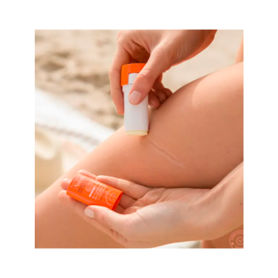 Bálsamo labial em bastão com embalagem laranja e branca aplicado na pele de uma perna