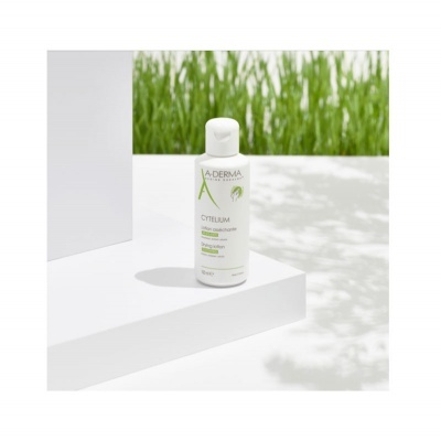 Frasco branco de A-DERMA na superfície branca com relva verde ao fundo