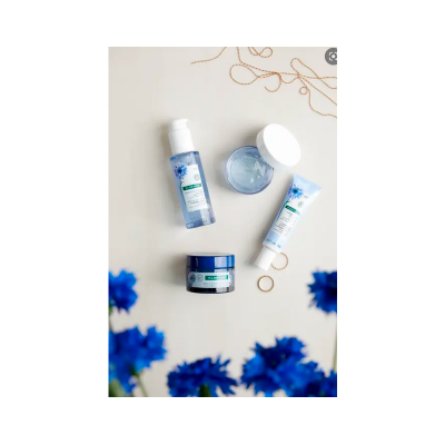 Produtos de cuidados para o rosto em embalagens azuis e brancas sobre uma superfície clara com flores azuis.