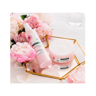 Produtos cosméticos Klorane com extrato de pivoine em fundo branco com flores e base espelhada dourada