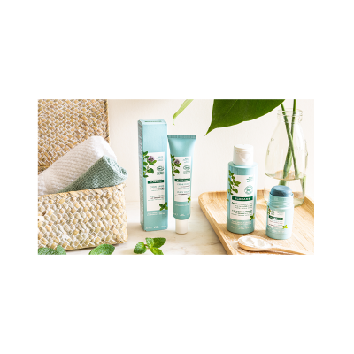 Produtos de cuidado corporal com embalagens azuis claras e brancas com folhas verdes próximos a toalhas numa cesta e jarra com água.