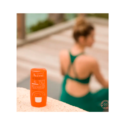 Frasco laranja de protetor solar Avène FPS 50+ sobre superfície clara com pessoa ao fundo