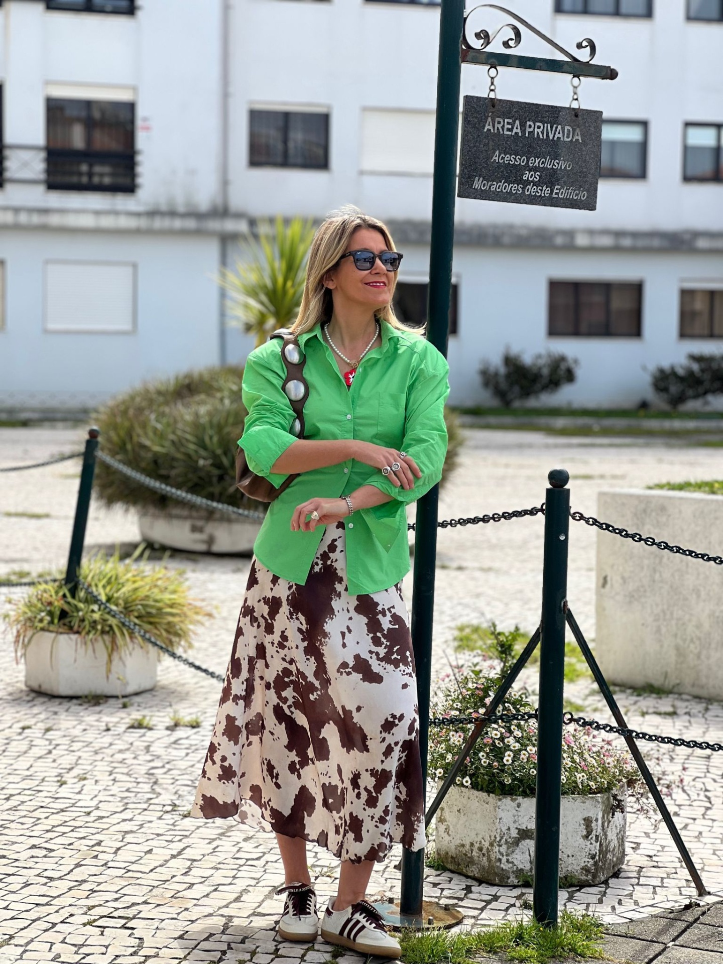Mulher com camisa verde e saia estampada em rua com prédio ao fundo