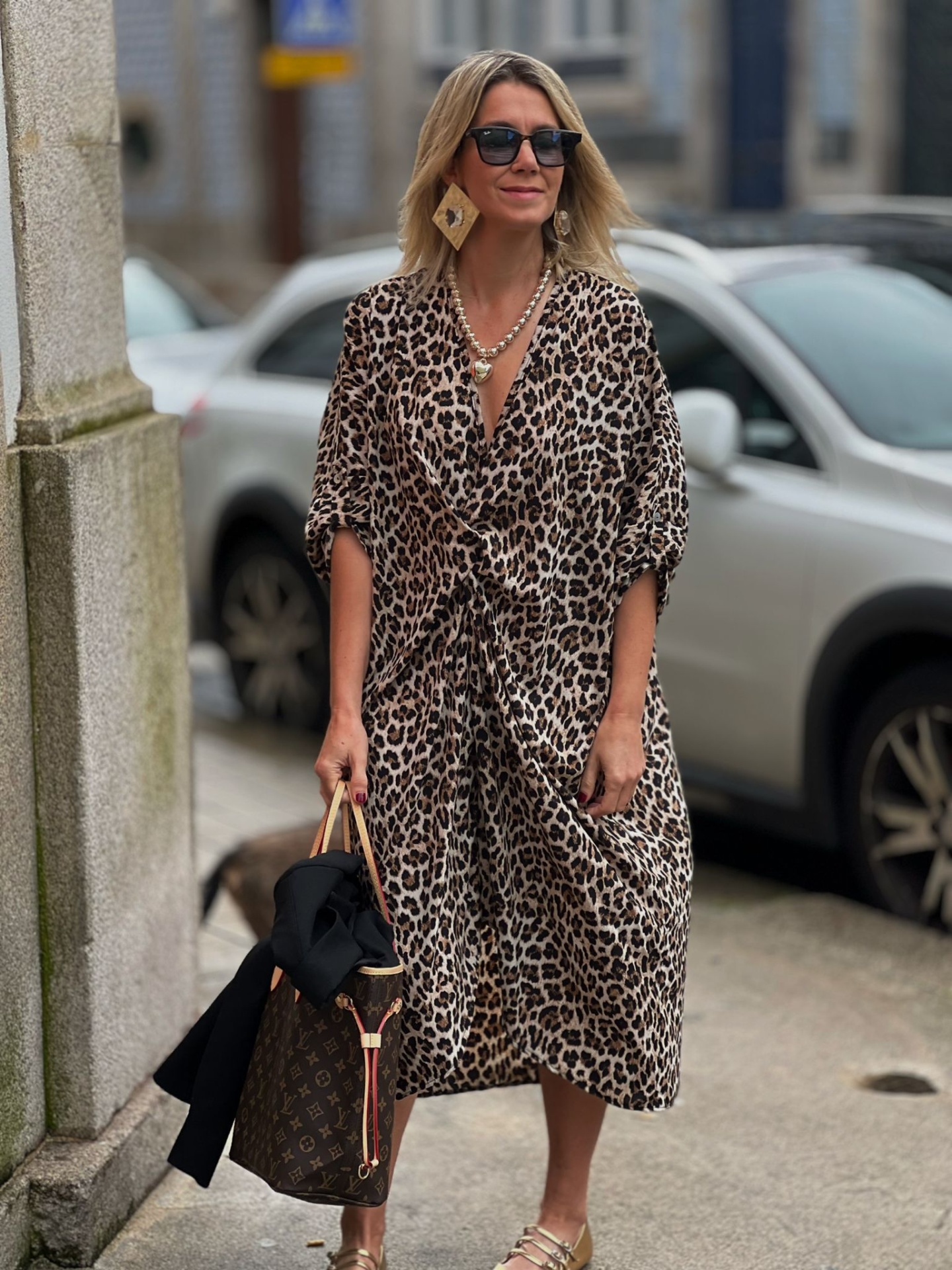 Mulher com vestido midi estampado animal print, sandálias douradas e bolsa castanha com padrão geométrico