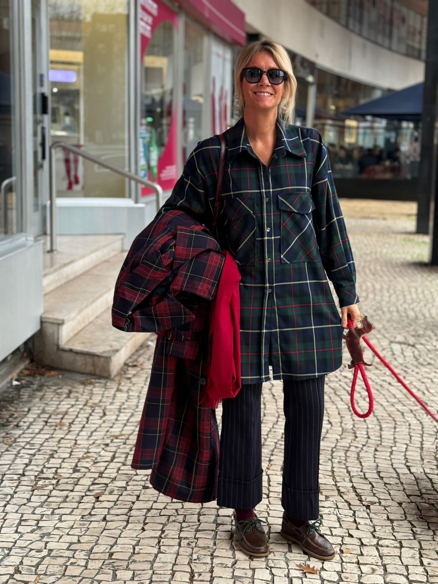 Mulher com camisa comprida xadrez e casaco xadrez segurado ao lado