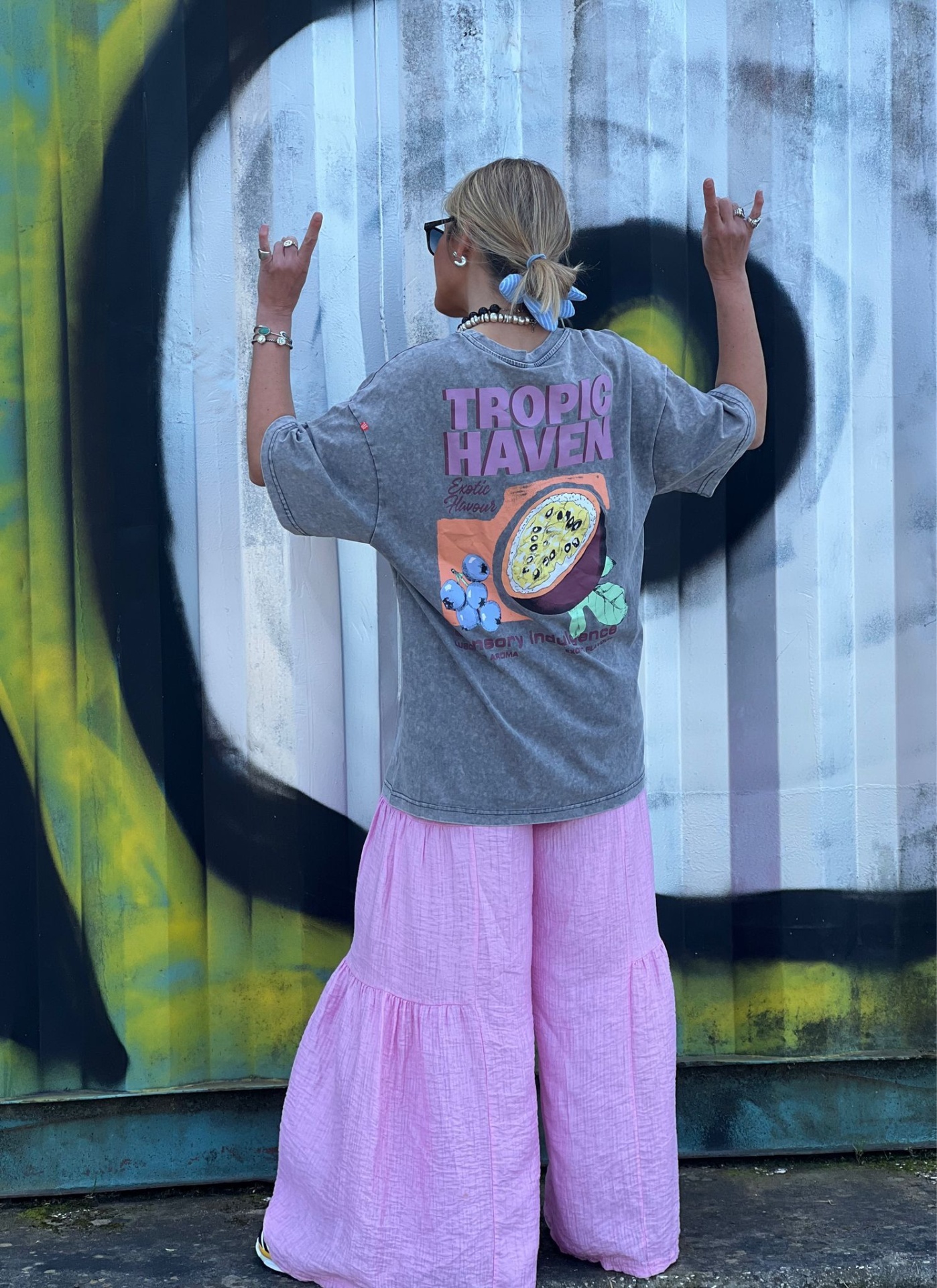 Pessoa de costas usando t-shirt cinzenta com estampa colorida e calças largas rosa claro