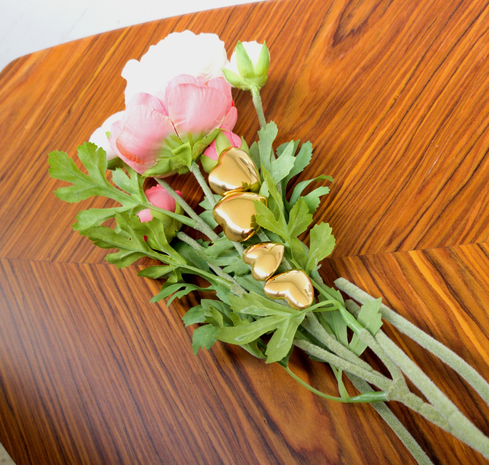 Ramo de flores artificiais com sinos dourados sobre mesa de madeira