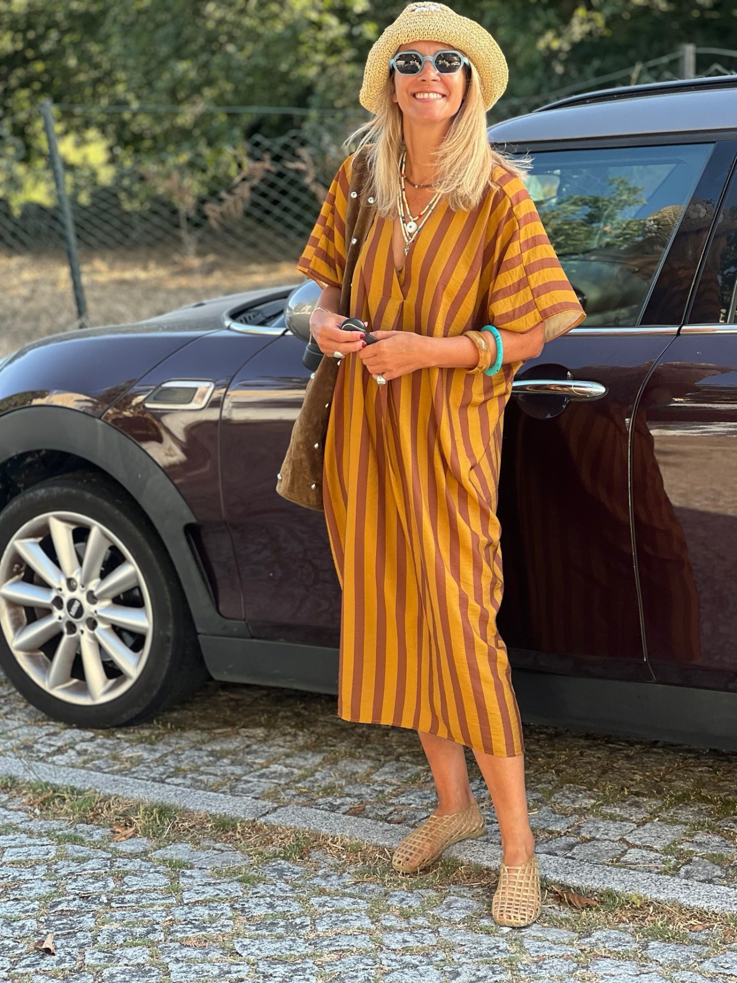 Mulher com vestido riscado castanho e laranja junto a carro preto