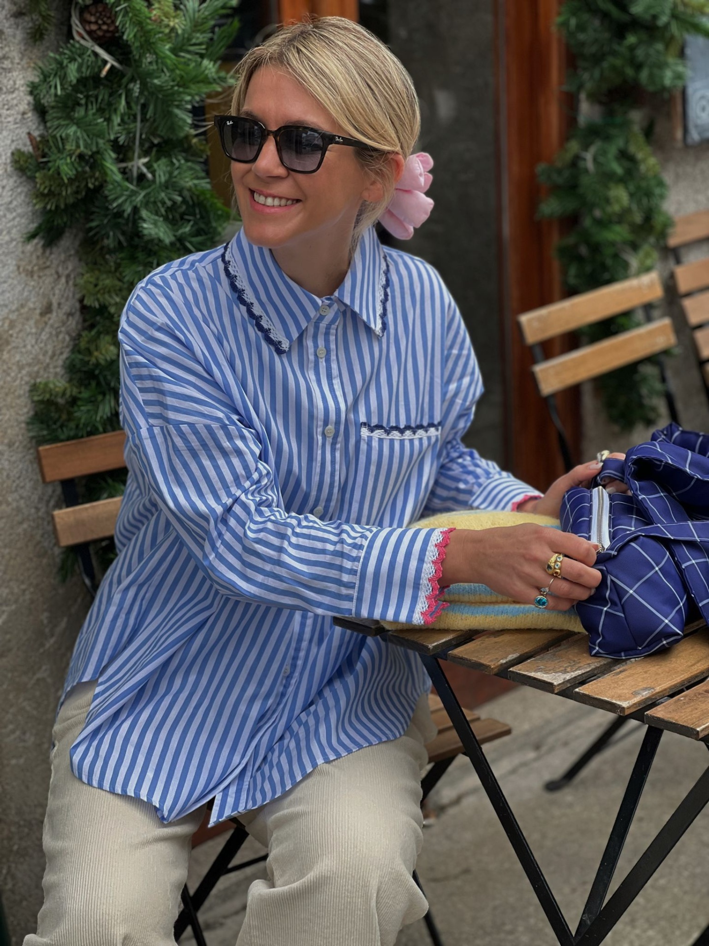 Camisa azul com riscas brancas e detalhes pretos e rosa, ao ar livre, mulher sentada