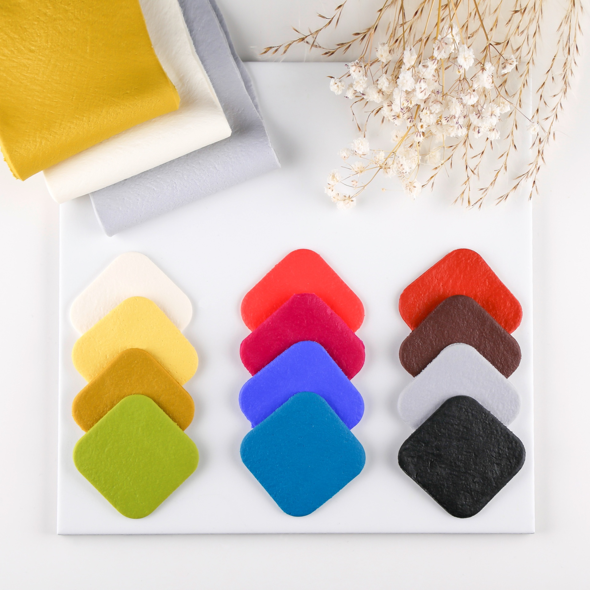 Amostras coloridas de tecido organizadas em colunas com raminhos secos ao fundo