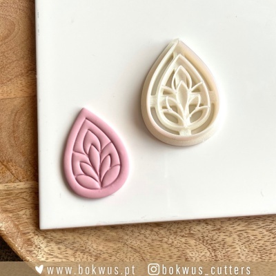 Dois cortadores de massa com padrão de folhas, rosa e branco, sobre tabuleiro de madeira.