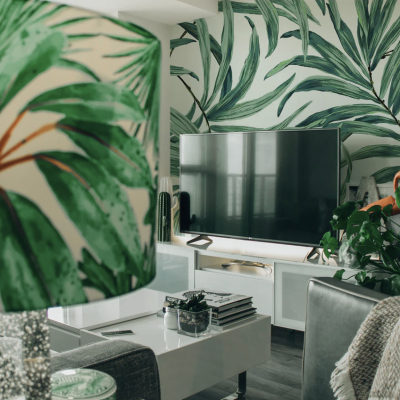 sala de estar com televisão, móveis brancos, plantas e papel de parede com folhas verdes