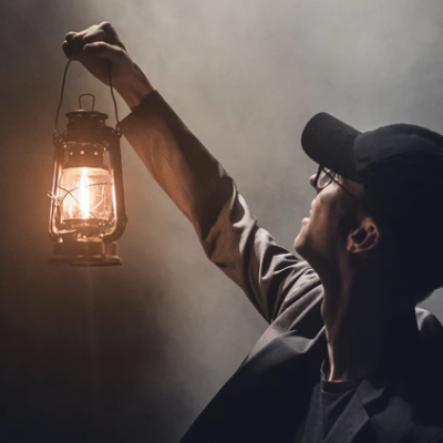 Homem segurando lanterna antiga acesa com fundo escuro