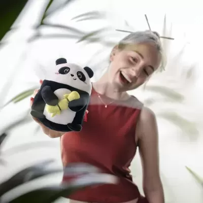 Brinquedo de peluche panda segurando banana nas mãos de jovem com blusa vermelha
