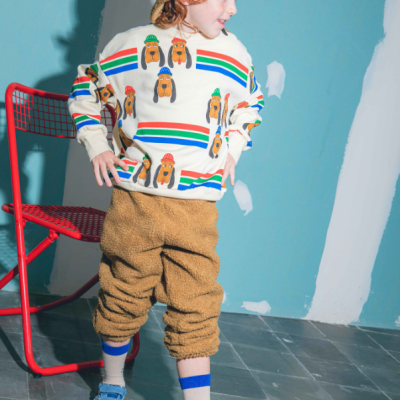 Criança com roupa colorida e chapéu felpudo a lado de cadeira vermelha