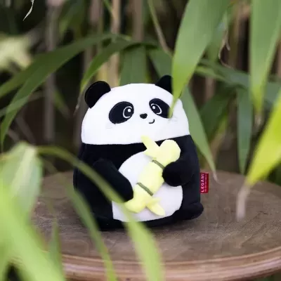 Pelúcia de panda segurando bambu sobre tabuleiro de madeira com folhas verdes ao fundo
