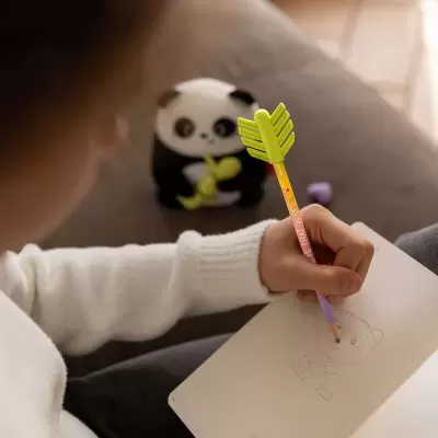 Lápis colorido com borracha verde em forma de folha e mão de criança a desenhar panda num caderno