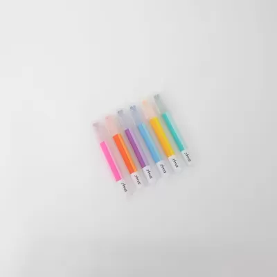 Seis marcadores de texto em várias cores pastel com tampas transparentes dispostos em fundo branco.