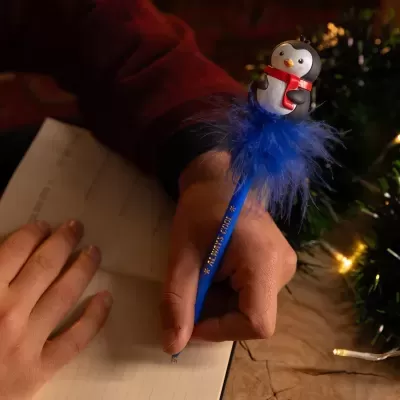 Caneta azul com pinguim decorativo e penas azuis a escrever num caderno