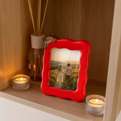 Moldura vermelha com urso castanho e foto de casal na prateleira com velas.