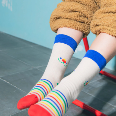 Meias brancas com riscas coloridas e detalhes azuis e vermelhos, usadas com calças peludas castanhas sentado numa cadeira vermelha.
