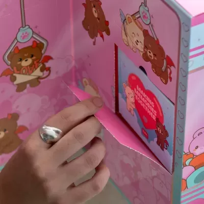 Mão abrindo caixa rosa com ursos anjos e diabinhos e texto MAKING MEMORIES TOGETHER