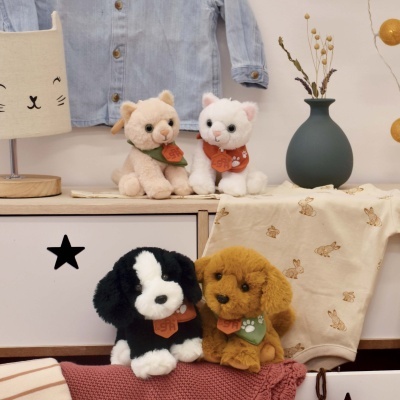 Quatro peluches de gatos e cães com bandanas coloridas sobre móvel de madeira com candeeiro e vaso.