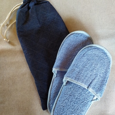 Chinelos azuis claros felpudos com bolsa azul escura sobre superfície bege