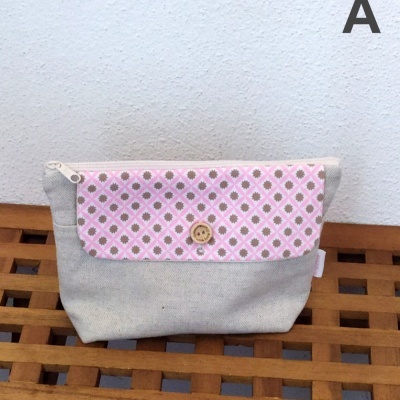 Necessaire bege com pala rosa padronizada e botão de madeira sobre superfície de madeira.