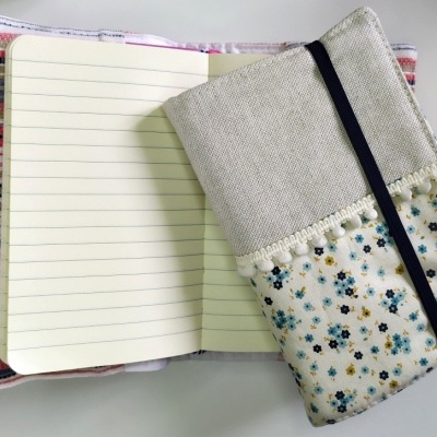 Dois cadernos, um aberto com capa listrada e outro fechado com capa floral e elástico preto