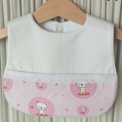 Babete de bebé branco e rosa com padrão de ursos e pássaros em cabide de madeira