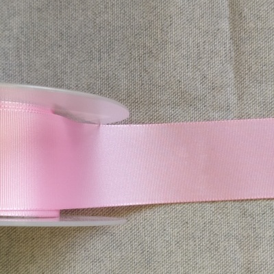 Rolo de fita de cetim rosa claro sobre fundo cinza têxtil com texto 'Rosa'