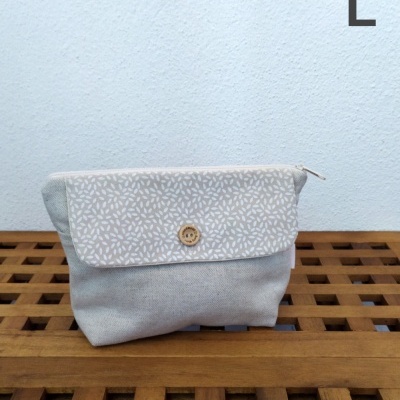 Bolsa pequena cinzenta com aba estampada e botão de madeira, colocada sobre superfície de madeira.