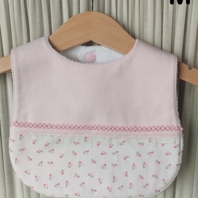 Babete de bebé cor de rosa com padrão floral pendurado num cabide