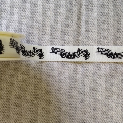 Fita branca com notas musicais pretas enrolada em carretel sobre tecido cinzento