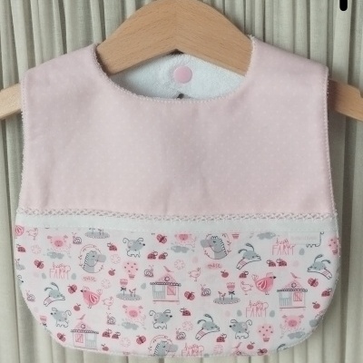 Babete de bebê rosa e branca com desenho infantil pendurada em cabide de madeira