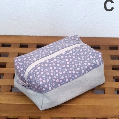 Necessaire retangular em tecido floral lilás e rosa com base cinzento claro e fecho branco sobre superfície de madeira