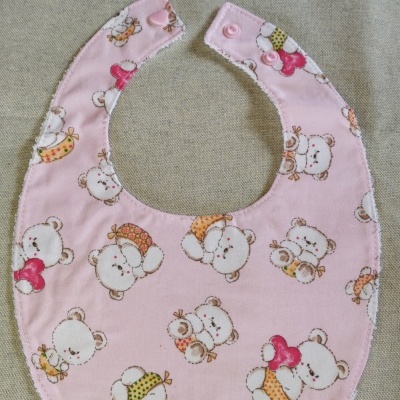 Babete para bebé cor de rosa com padrão de ursos brancos a segurar corações.
