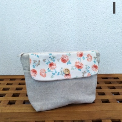 Necessaire cinzenta com aba branca floral e botão de madeira sobre madeira