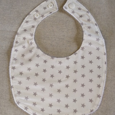 Babete branco com estrelas cinzentas e fecho por botões em fundo cinza